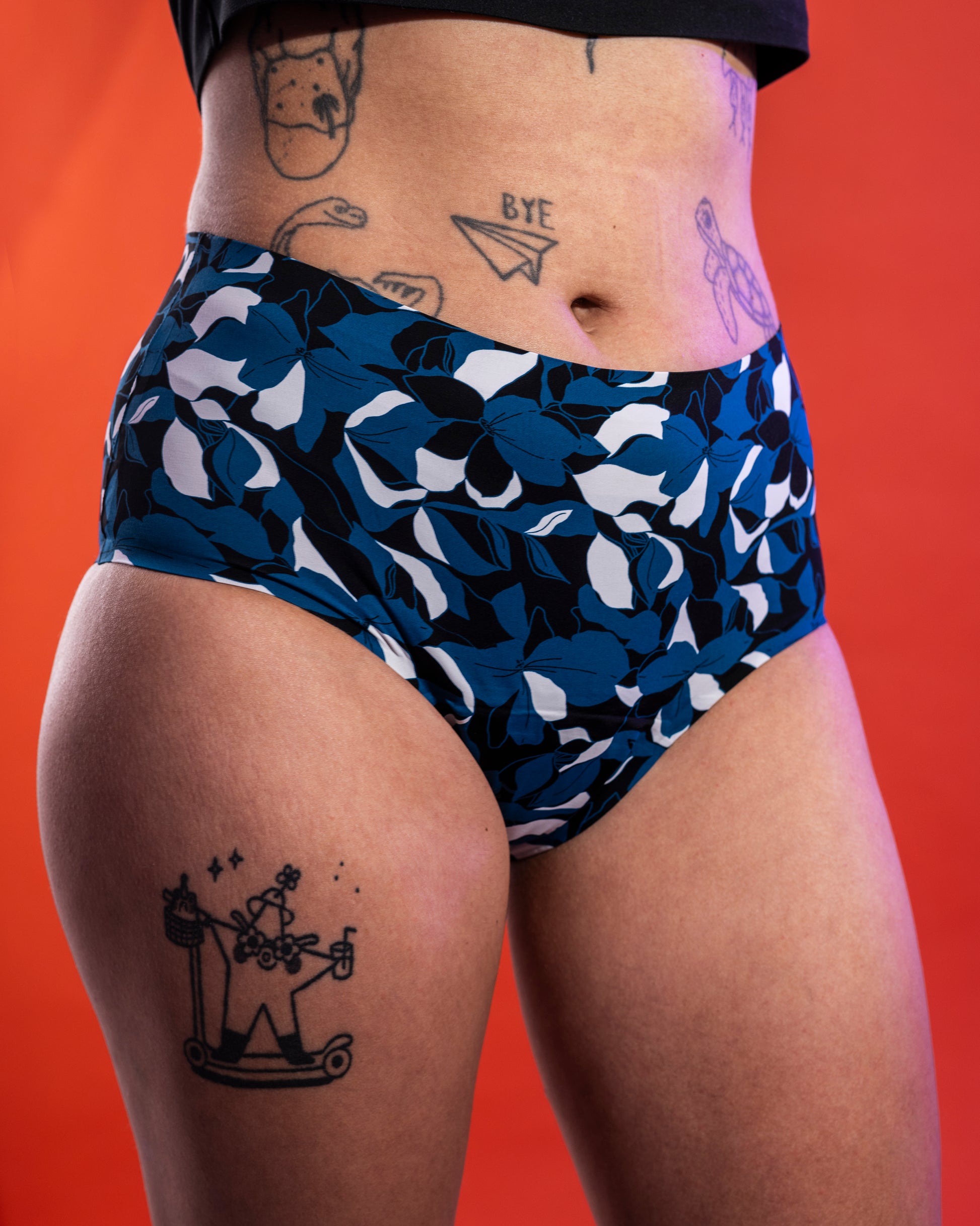 Modell trägt Blue Bloom Periodenunterwäsche frontal, hoher Bund, florales Muster auf Blau, roter Hintergrund